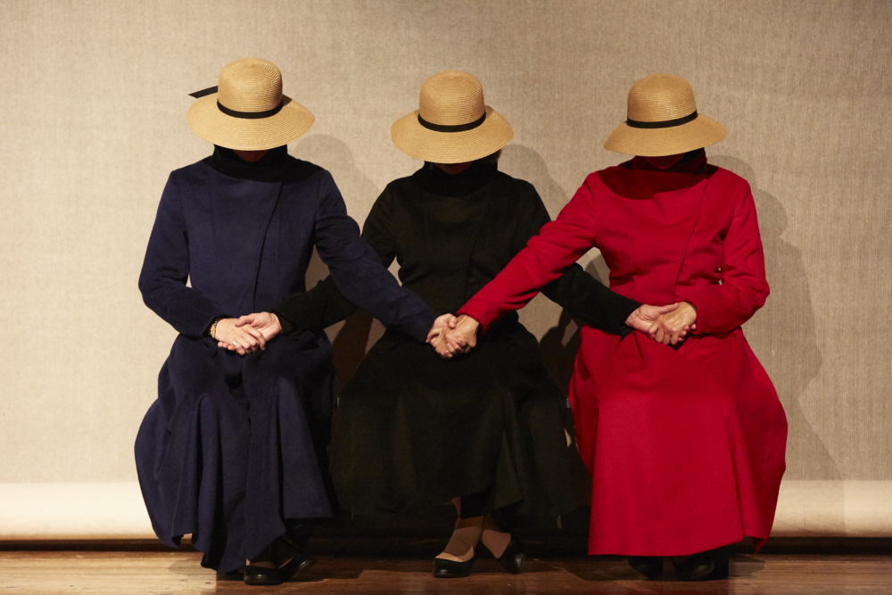 Adult woman reading from a book, audience members are seen in the foreground
