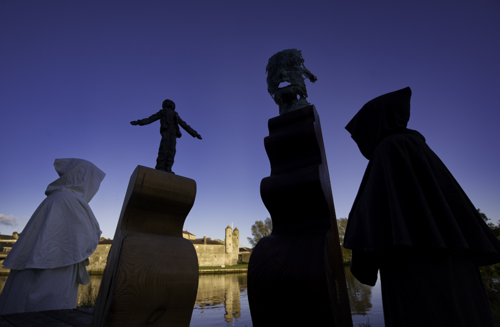 Person in white hood and three large chess pieces against a deep blue sky